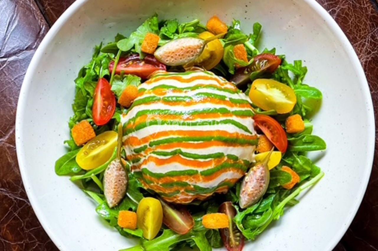 Salade colorée avec légumes frais, croûtons, quenelles et une boule garnie de sauce verte et orange.