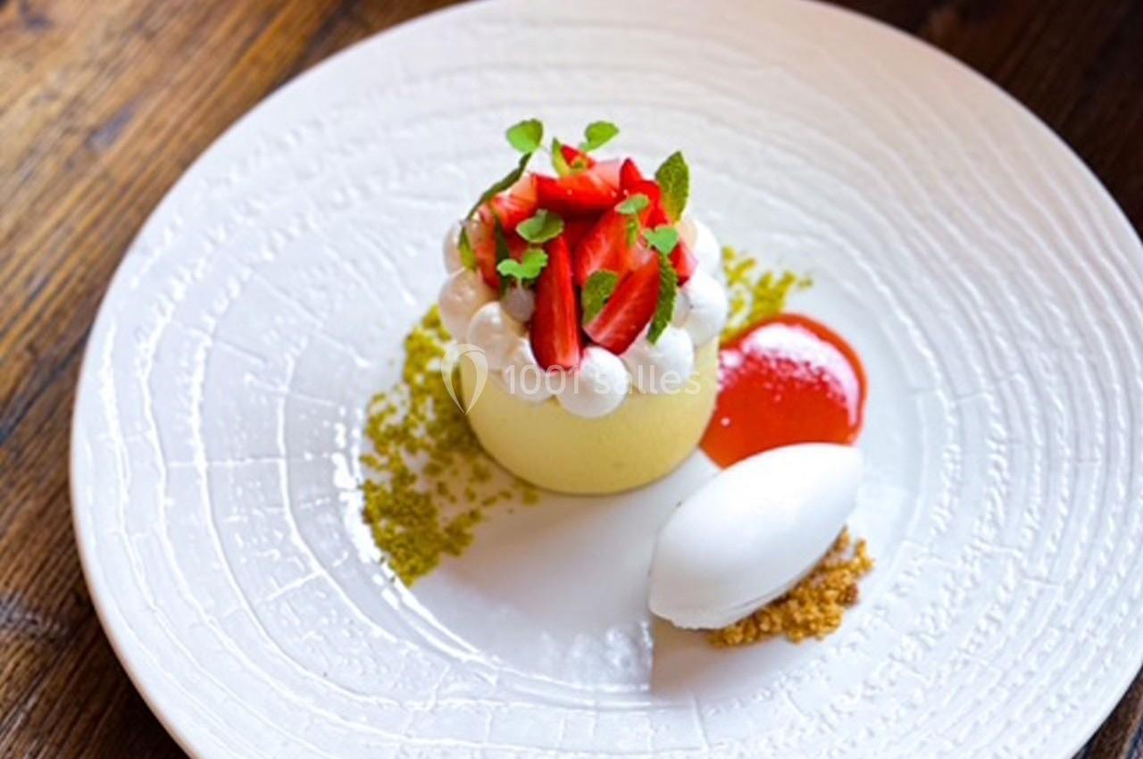 Dessert élégant composé d'une mousse garnie de fraises, crème, sorbet et coulis, présenté sur une assiette blanche.