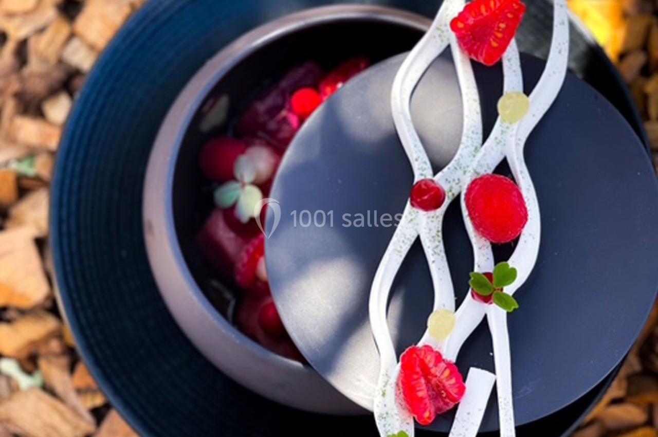 Dessert raffiné présenté dans un bol noir, décoré de fruits rouges, de crème blanche et de touches végétales.