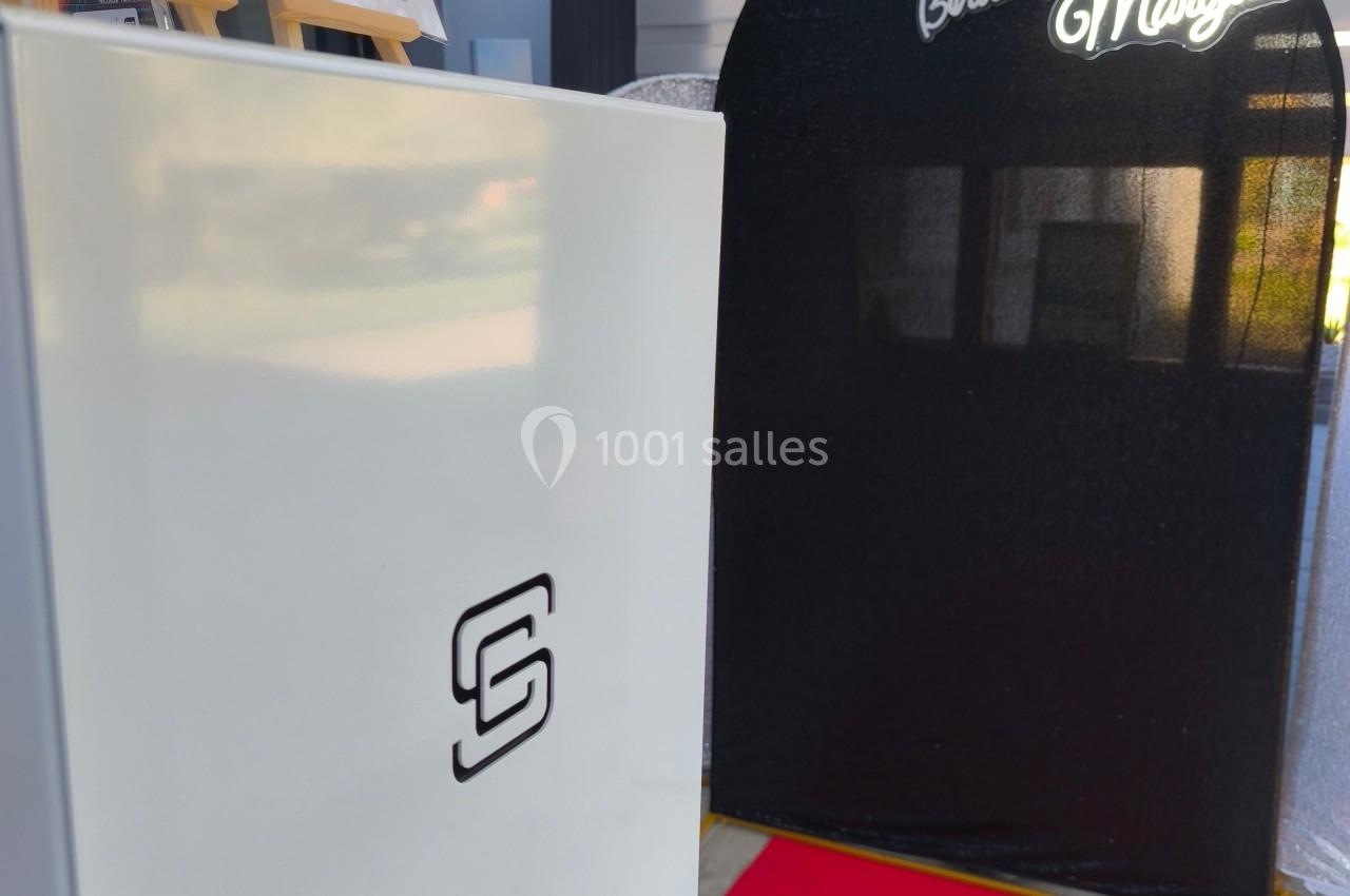 Photobooth avec fond noir ’Happy Birthday Margaux’, tapis rouge et borne photo blanche dans un espace intérieur.