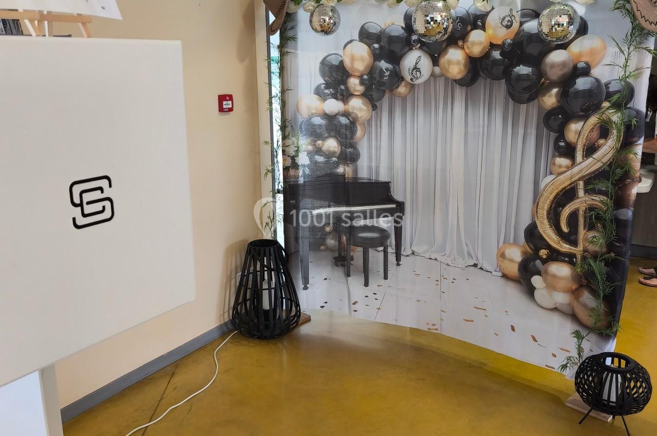 Décor festif avec ballons noirs, dorés et blancs, piano noir et arche ornée de notes de musique.