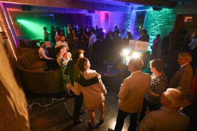 Miniature Mariage Abbaye du Trésor Des personnes dansent et discutent dans une salle éclairée par des lumières colorées lors d'un événement festif.