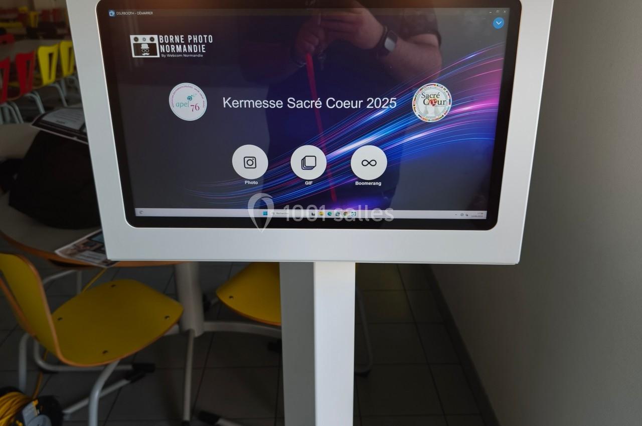 Borne photo interactive sur pied avec écran tactile affichant un menu pour un événement nommé ’Kermesse Sacré Coeur 2025’.