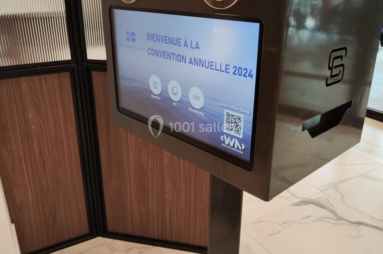 Borne interactive affichant un écran de bienvenue pour une convention annuelle, installée dans un espace intérieur moderne.