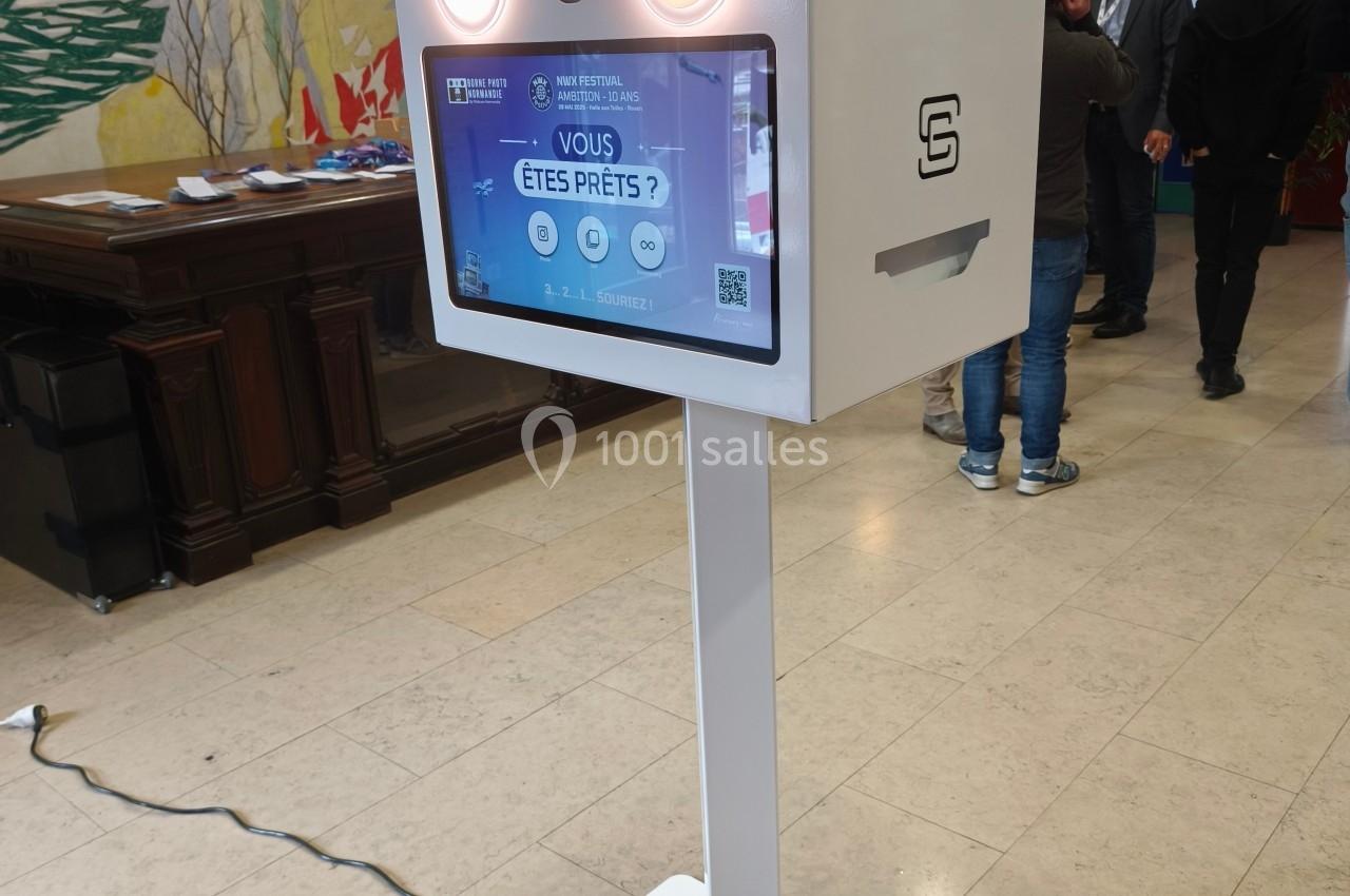 Borne photo interactive avec écran tactile et éclairage intégré, installée dans un hall à la décoration murale colorée.