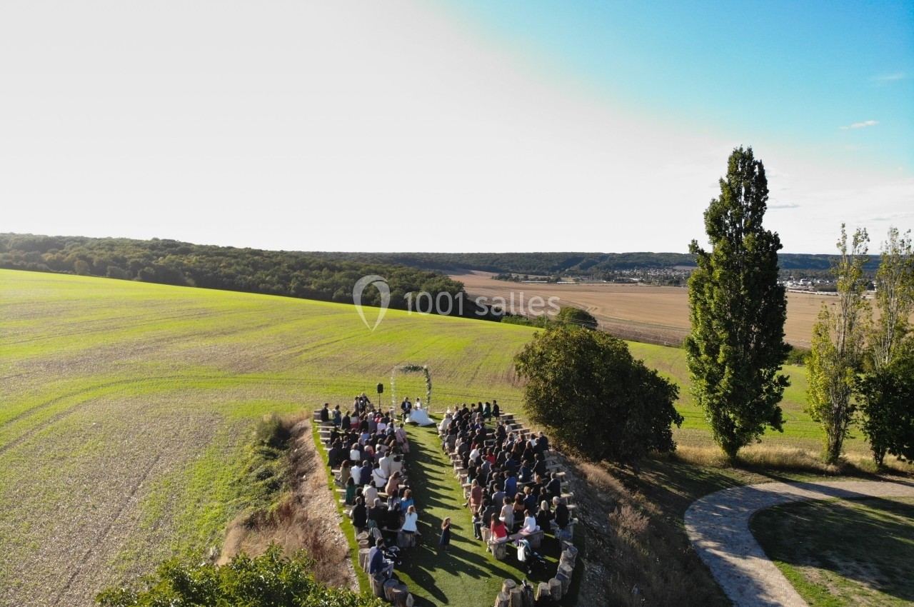 Cérémonie en plein air avec des invités assis, entourée de champs et d'arbres sous un ciel dégagé.