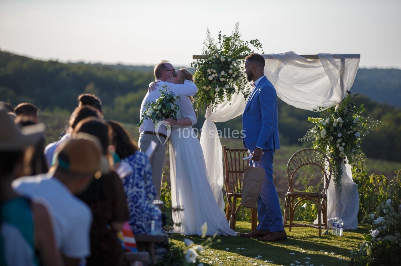 Un couple s'embrasse sous une arche décorée de fleurs lors d'une cérémonie de mariage en plein air.