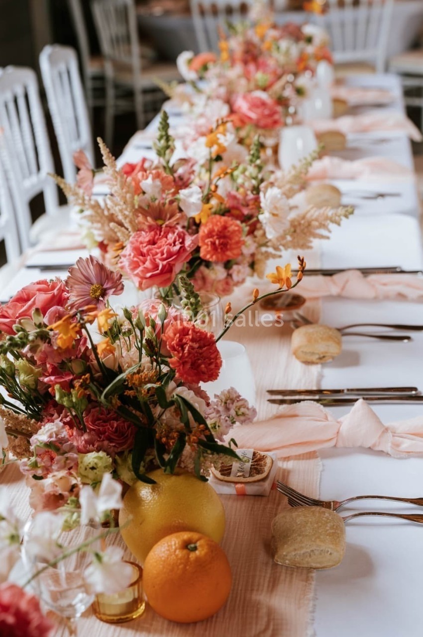 Table décorée avec des fleurs colorées, des fruits et des couverts disposés pour un repas festif.