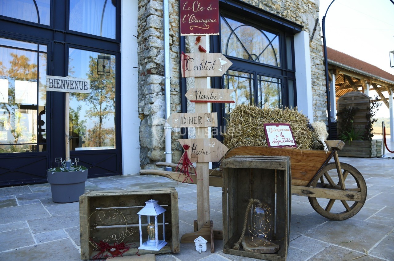 Panneau en bois indiquant différentes directions devant une bâtisse en pierre, décoré avec des caisses et une charrette.