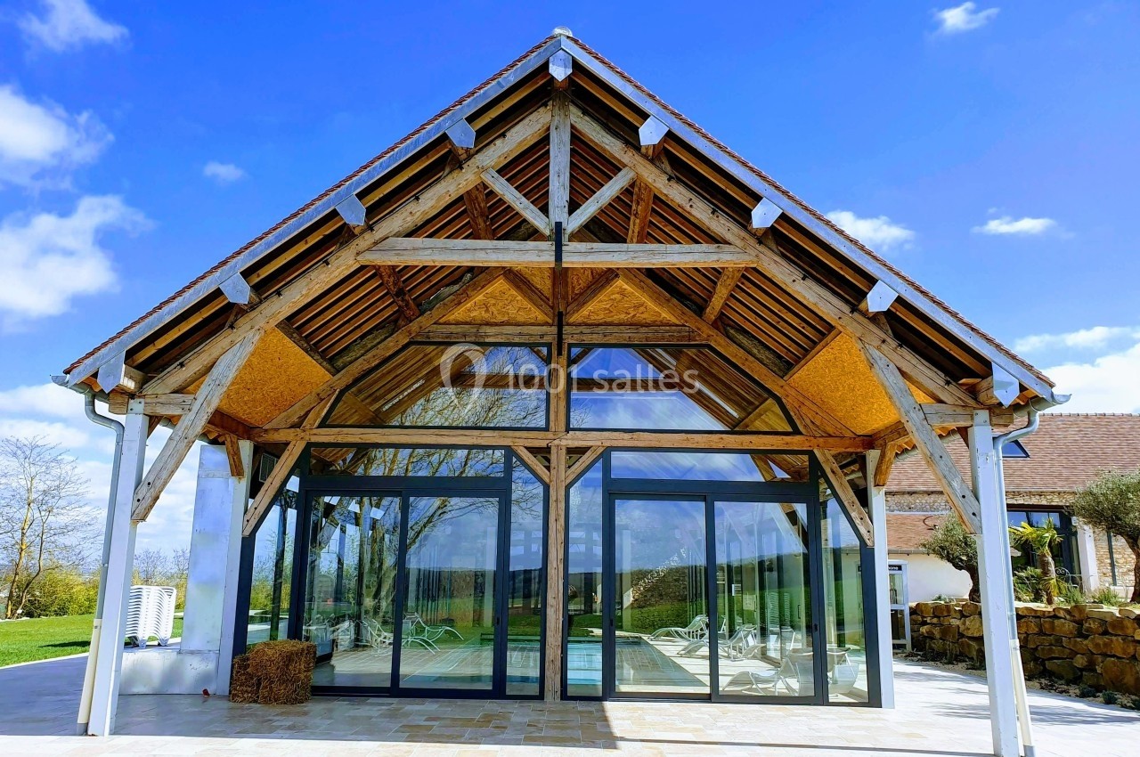 Structure en bois avec de grandes baies vitrées donnant sur un espace extérieur, sous un ciel bleu dégagé.
