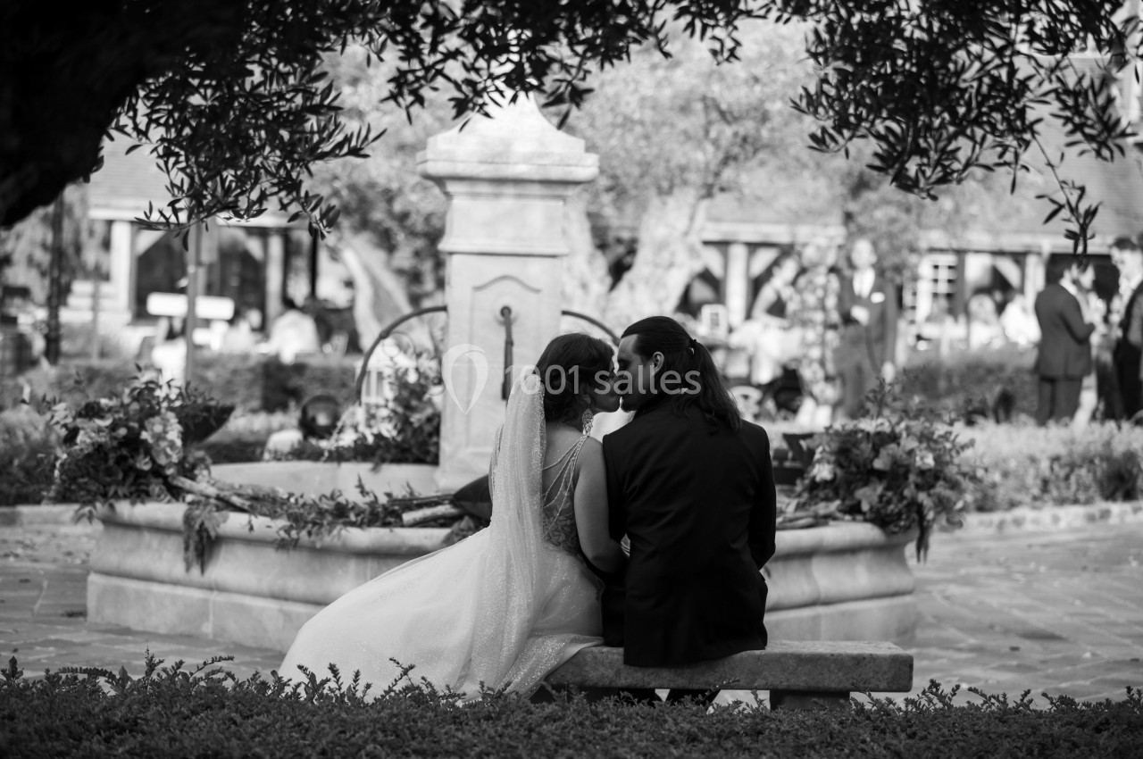 Un couple assis sur un banc près d'une fontaine dans un jardin, échangeant un moment intime.