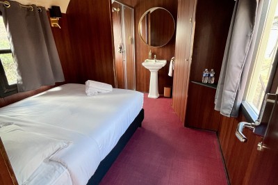 Chambre spacieuse sous combles avec poutres apparentes, lit double, coin salon coloré et grande baie vitrée.