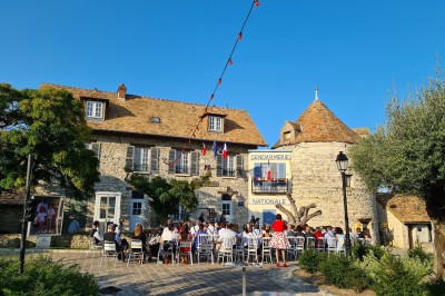 Chambre spacieuse sous combles avec poutres apparentes, lit double, coin salon coloré et grande baie vitrée.