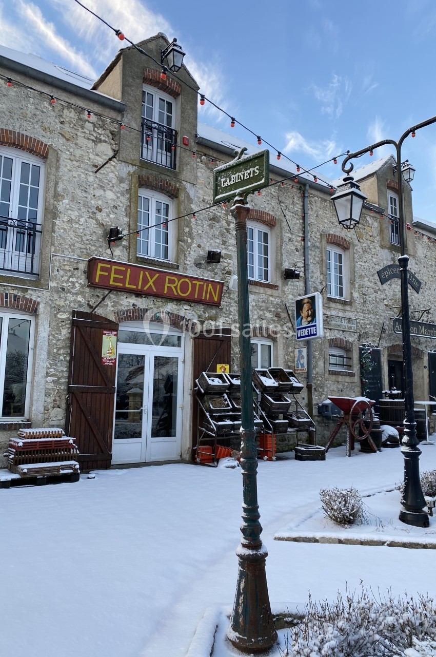 Façade d'une boutique en pierre avec des étals extérieurs, sur une rue enneigée bordée de lampadaires.