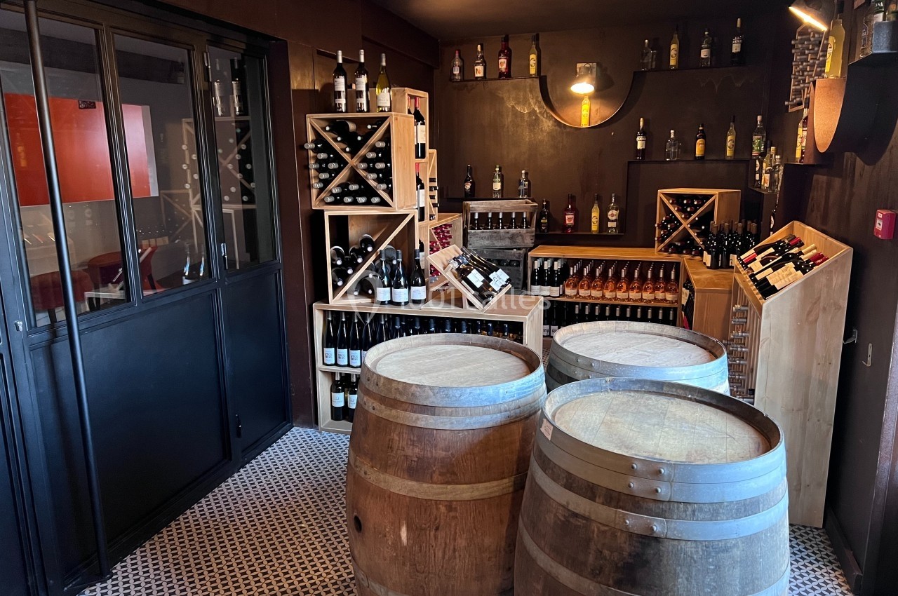 Cave à vin avec étagères remplies de bouteilles, trois tonneaux en bois au centre et éclairage tamisé.