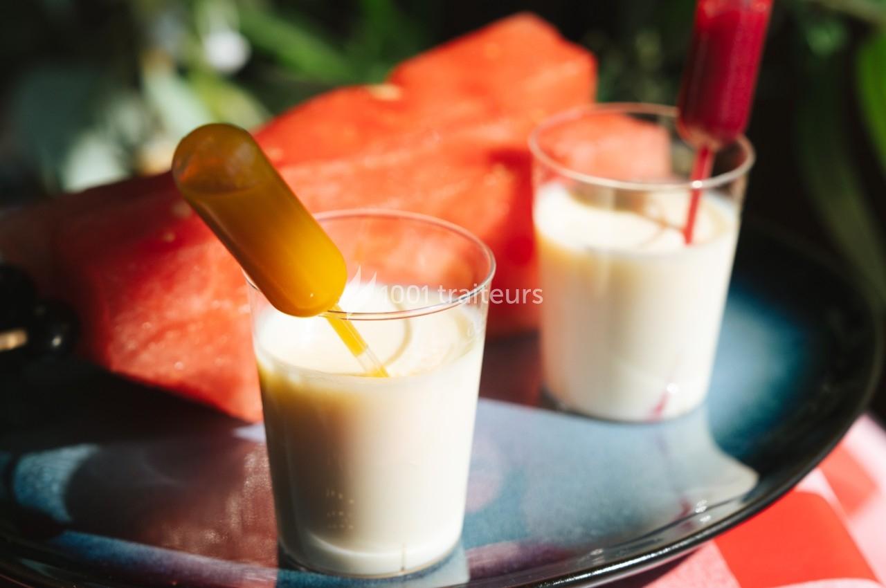 Deux verrines de yaourt avec pipettes colorées, posées sur une assiette près de tranches de pastèque.