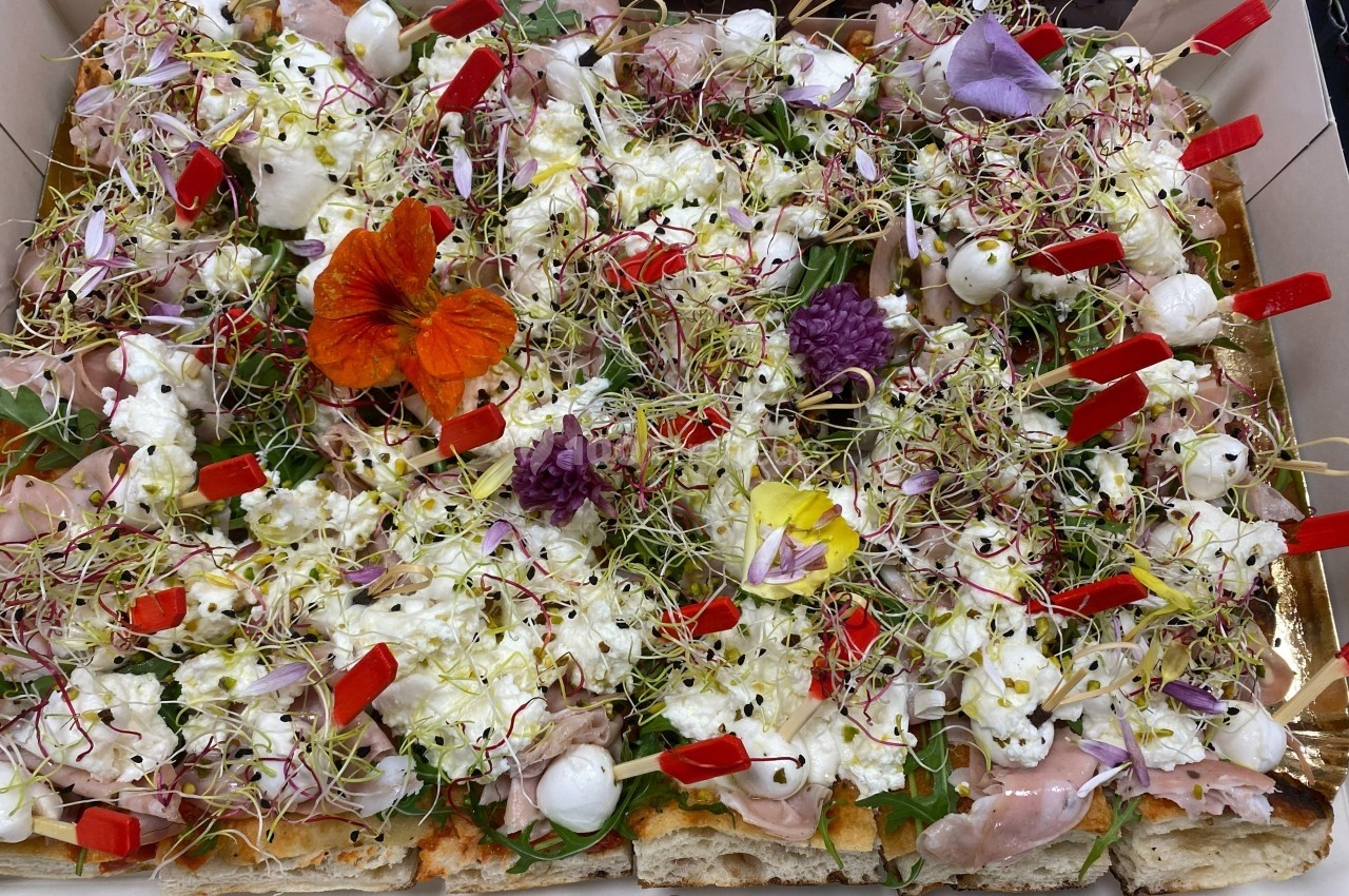 Pizza garnie de fleurs comestibles, mozzarella, jambon, pousses germées et brochettes individuelles.