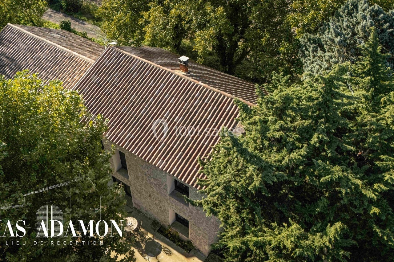 Vue aérienne d'un bâtiment en pierre entouré de grands arbres, avec un toit en tuiles rouges.