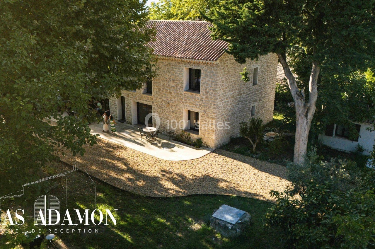 Vue aérienne d'une maison en pierre entourée d'arbres avec une allée en gravier et une terrasse aménagée.
