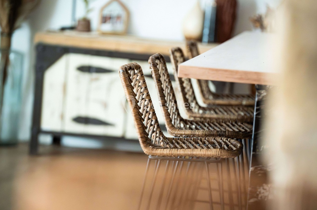 Chaises en rotin alignées autour d'une table en bois, avec un buffet flou en arrière-plan.