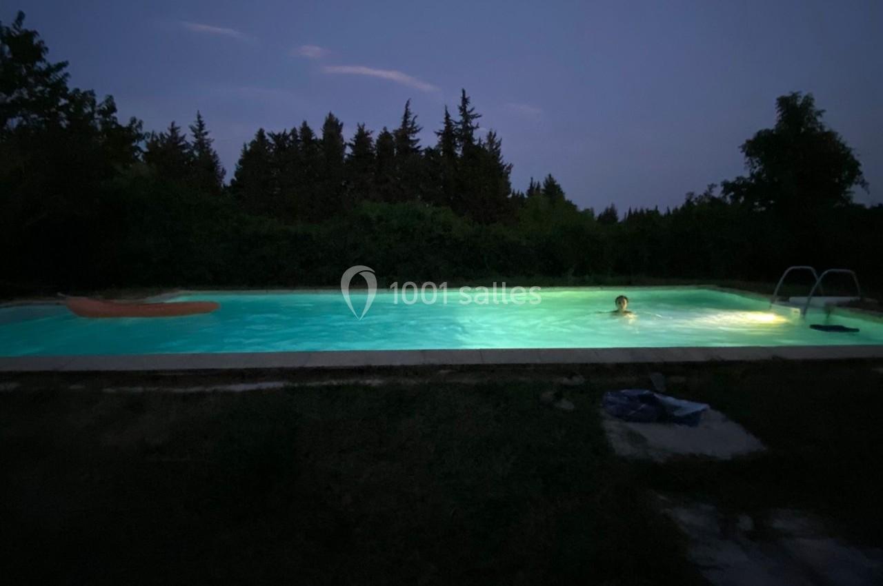 Piscine éclairée dans l'obscurité, entourée de végétation et d'arbres, avec une personne nageant.