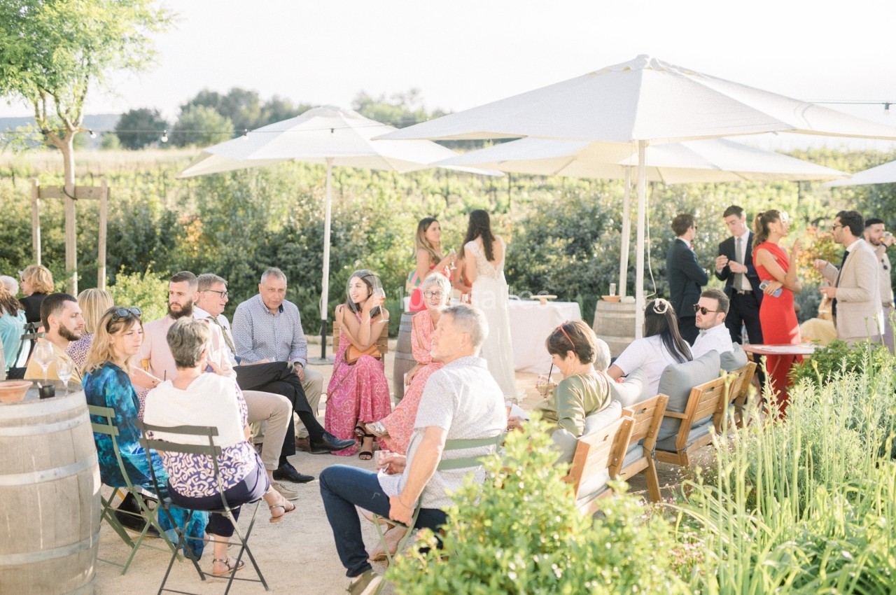 Groupe de personnes assises et discutant dans un jardin ensoleillé avec des parasols blancs.