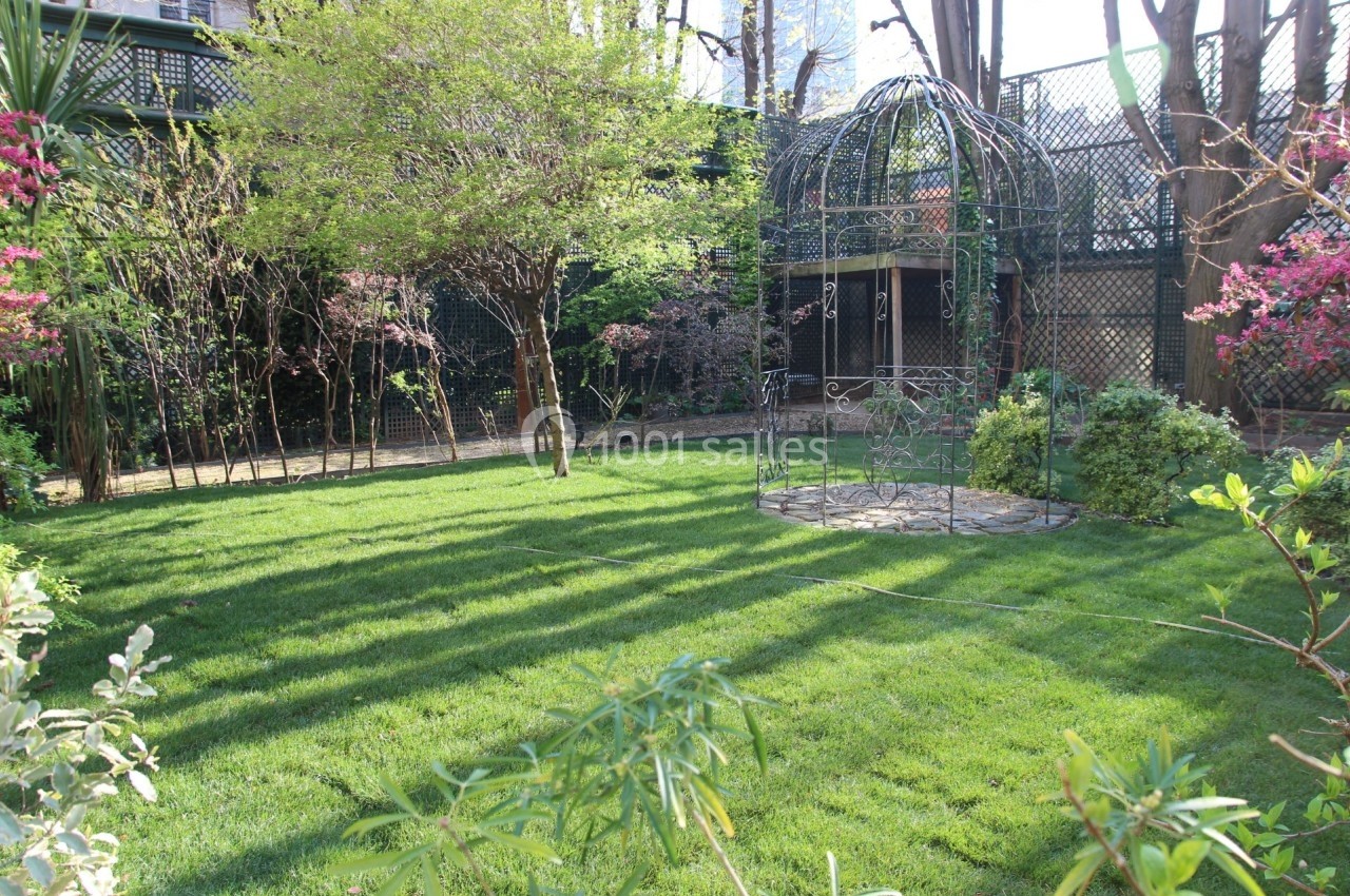Jardin verdoyant avec pelouse, arbres en fleurs et une structure métallique circulaire au centre.