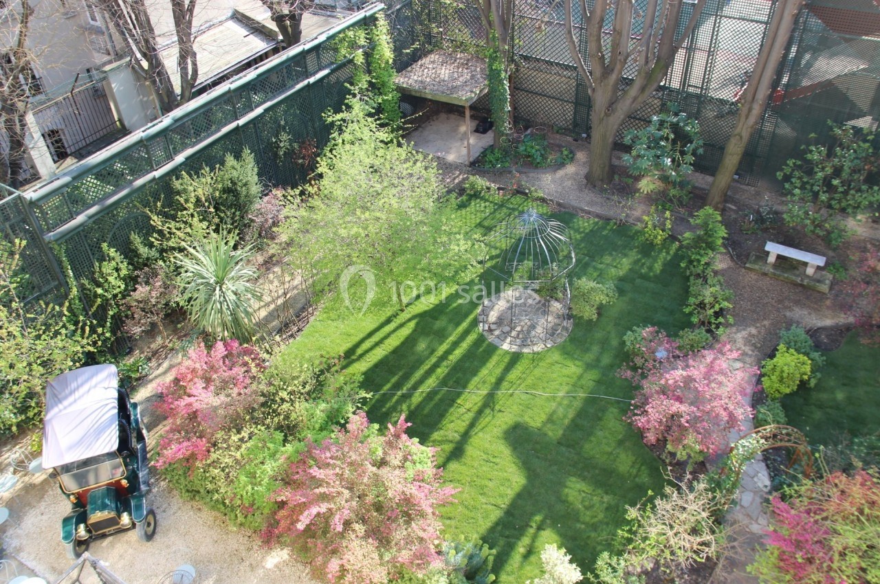 Vue aérienne d'un jardin verdoyant avec pelouse, arbustes fleuris, arbres et une structure métallique centrale.