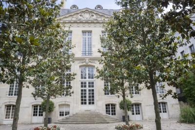 Vue d'un jardin verdoyant avec des arbres, des buissons et une grande cage métallique décorative au centre.