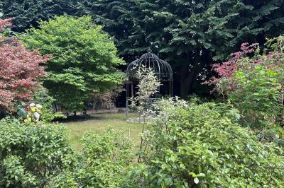 Vue d'un jardin verdoyant avec des arbres, des buissons et une grande cage métallique décorative au centre.
