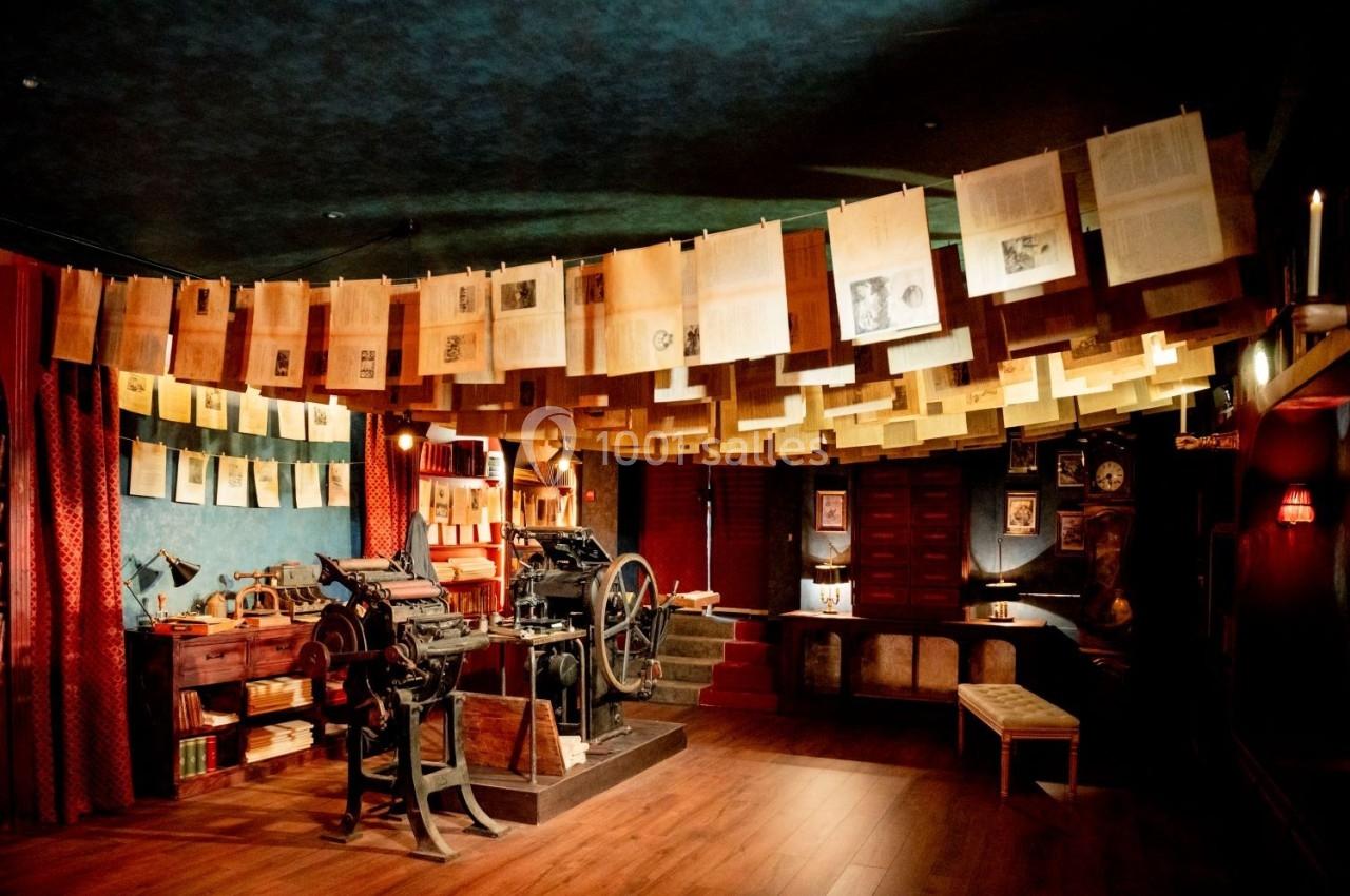 Atelier d'imprimerie ancienne avec une presse mécanique, des feuilles suspendues et un décor rétro en bois et tissu.