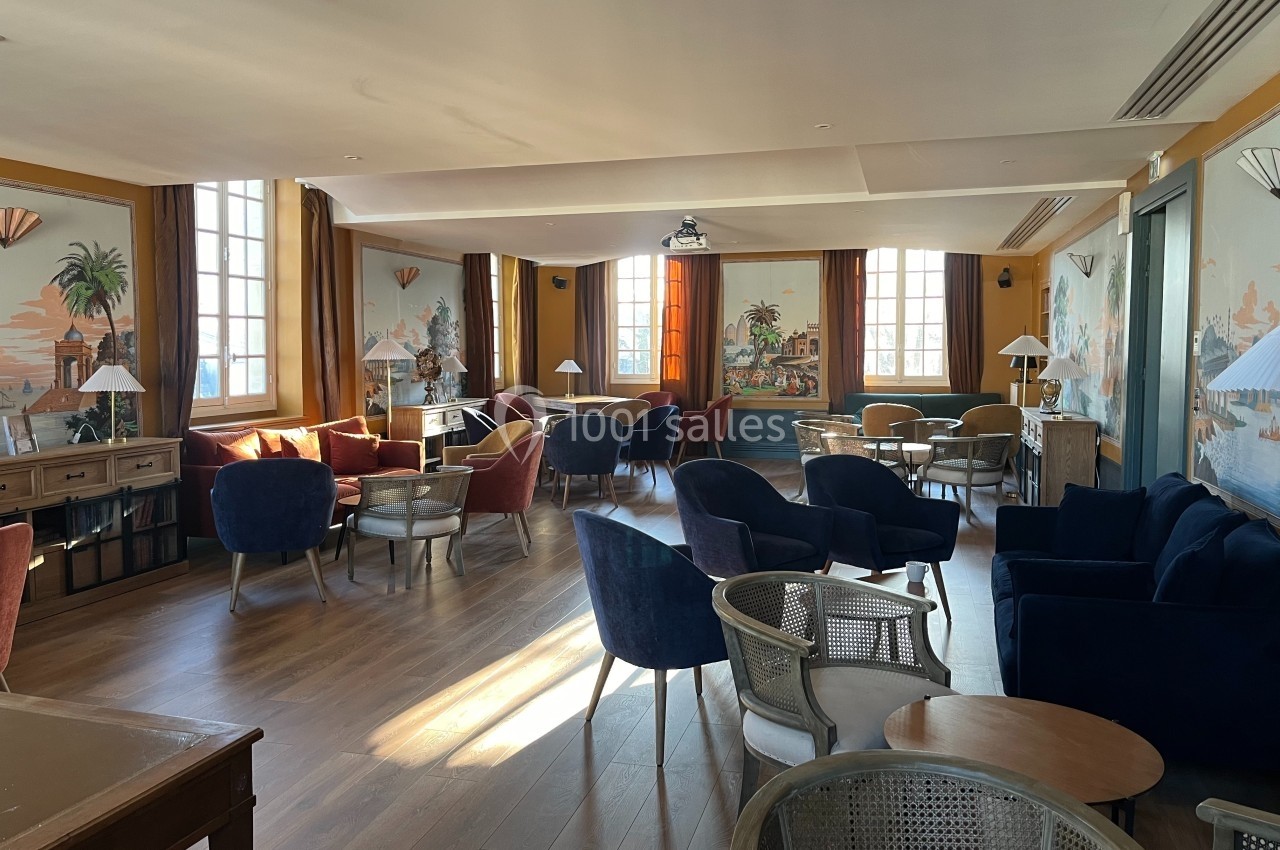 Salle lumineuse avec des fauteuils colorés, des tables en bois et des fresques murales représentant des paysages exotiques.