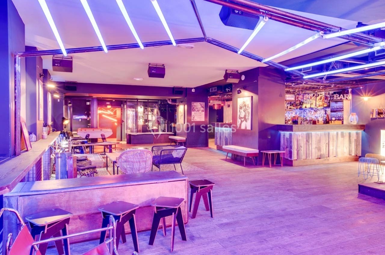 Intérieur d'un bar moderne avec éclairage néon violet, mobilier en bois et métal, et ambiance décontractée.