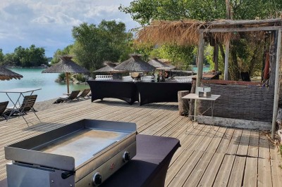 Chambre avec lit double bleu, tête de lit en rotin, décoration sobre et tableau représentant un ponton sur la mer.