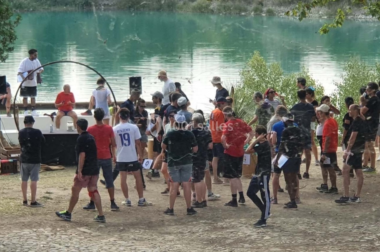 Groupe de personnes rassemblées en plein air près d'un lac, avec une scène et des intervenants en arrière-plan.