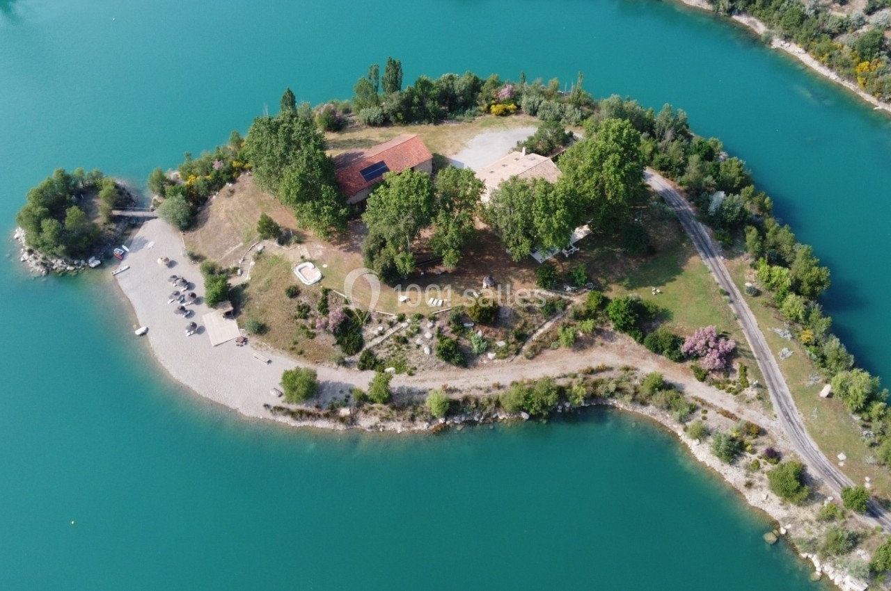 Vue aérienne d'une petite île boisée entourée d'eau turquoise, avec bâtiments et plages aménagées.