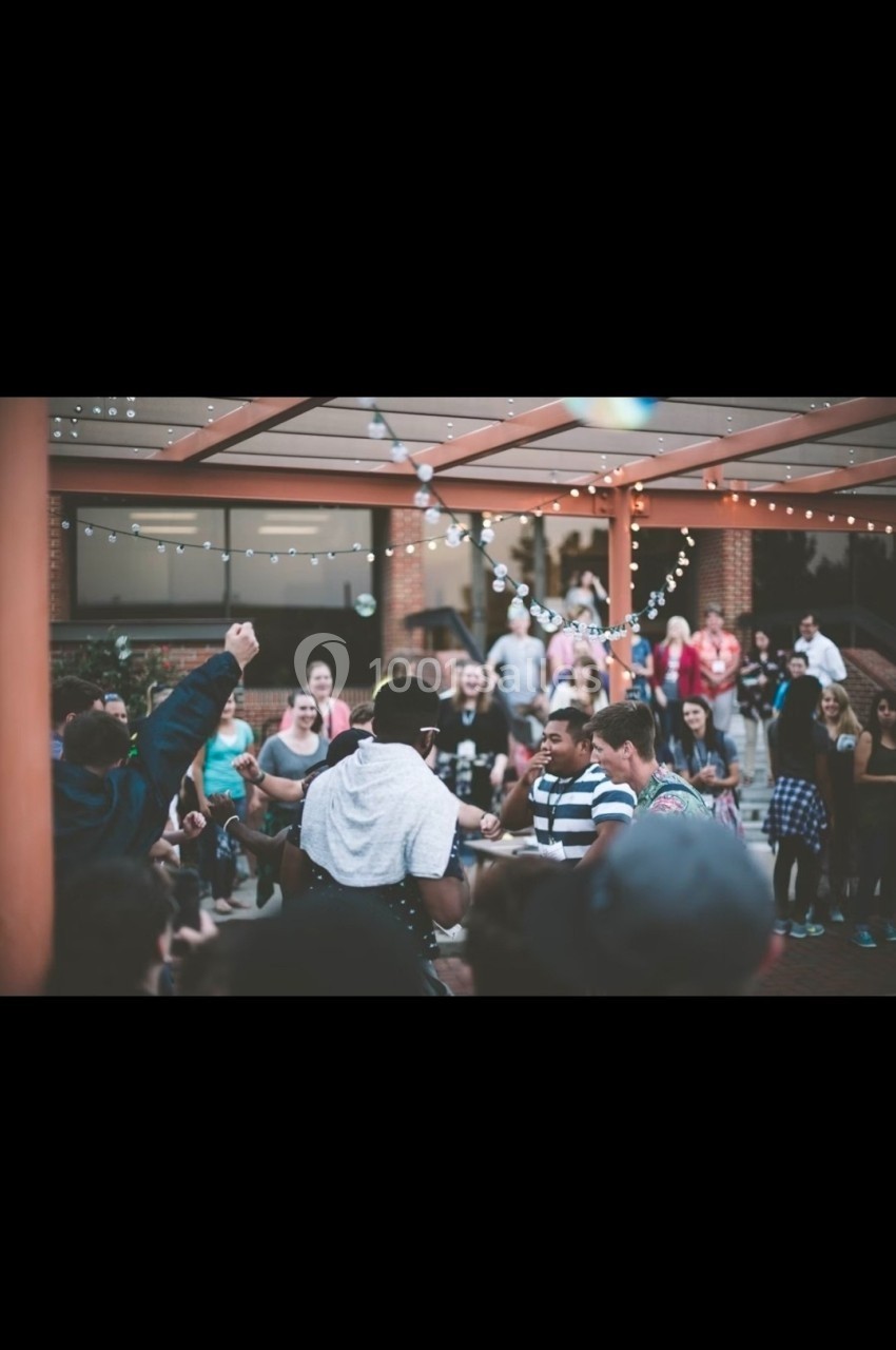Groupe de personnes rassemblées en extérieur sous des guirlandes lumineuses, certaines dansant ou discutant.