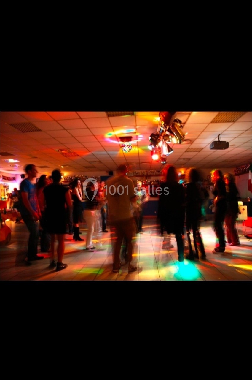Des personnes dansent sous des éclairages colorés dans une salle sombre avec un sol carrelé.