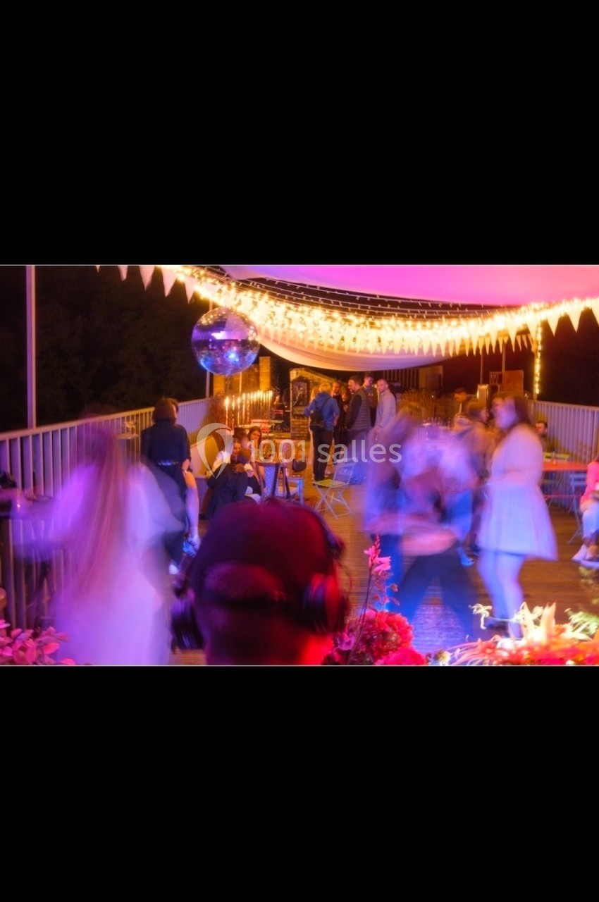 Personnes dansant et socialisant sur une terrasse éclairée par des guirlandes lumineuses, ambiance festive en soirée.