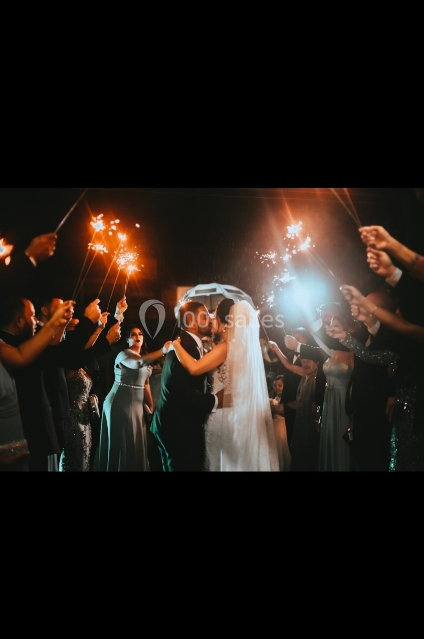 Un couple s'embrasse sous une arche, entouré d'invités tenant des cierges magiques allumés dans l'obscurité.
