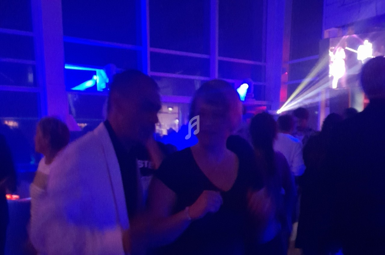 Des personnes dansent dans une ambiance festive avec des lumières colorées dans une salle sombre.