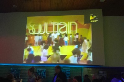 Miniature DJ Le Mée-sur-Seine (Seine-et-Marne) - Dj Urya #5 Une DJ en robe verte mixe de la musique sur une table de mixage dans un décor lumineux avec des fleurs de cerisier.