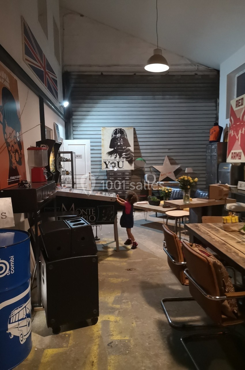 Un enfant joue sur un flipper dans un espace aménagé avec des affiches, meubles vintage et objets décoratifs.