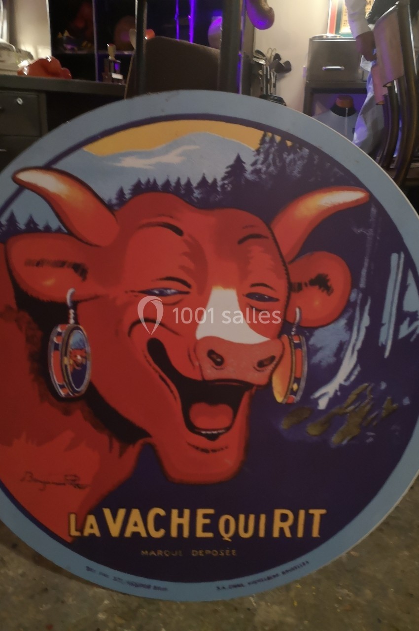 Affiche circulaire représentant une vache rouge souriante avec des boucles d'oreilles, logo ’La Vache qui Rit’.
