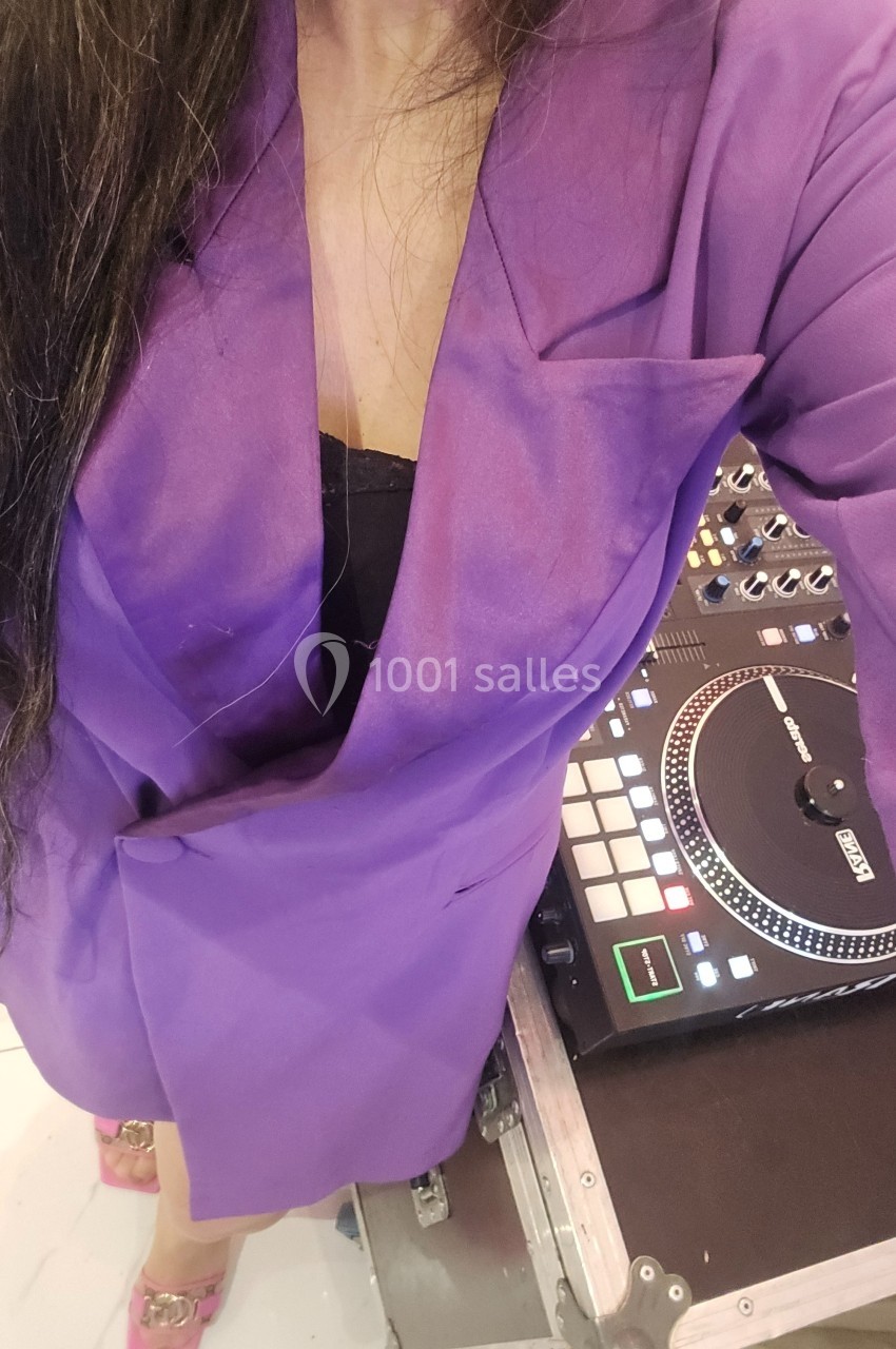 Femme en blazer violet debout près d'une table de mixage avec une platine vinyle.