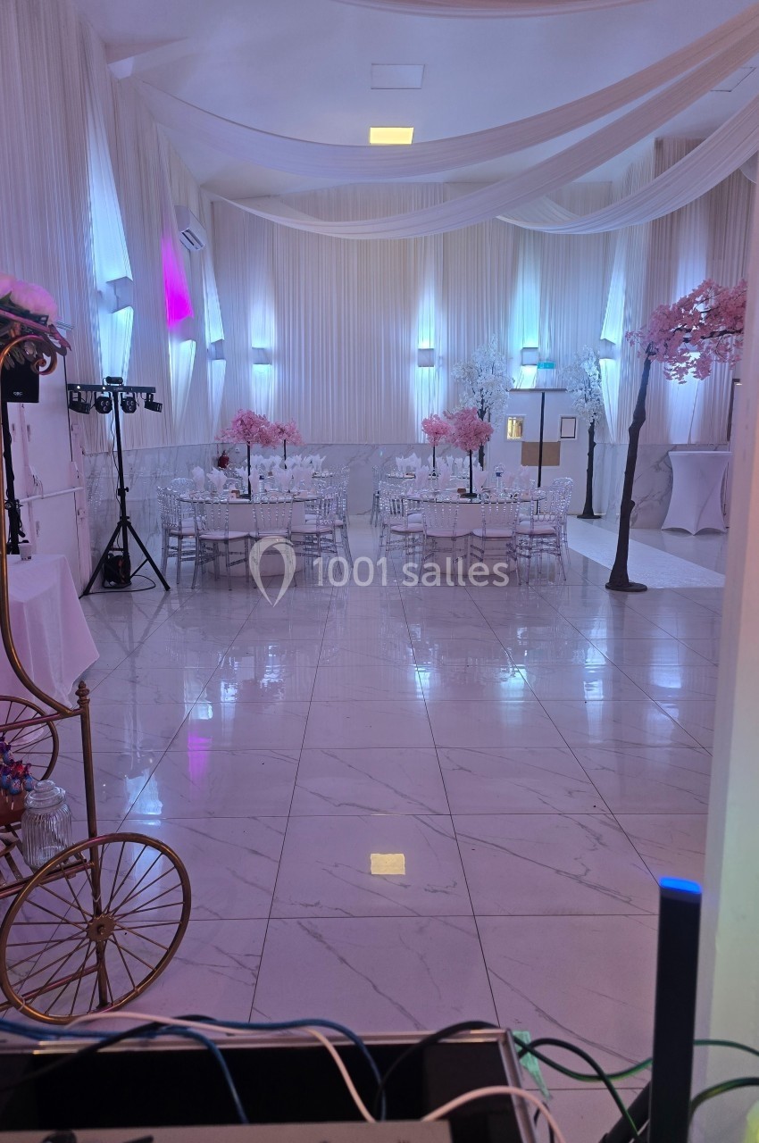 Salle de réception décorée avec des tables dressées, des arbres roses artificiels et un éclairage tamisé.