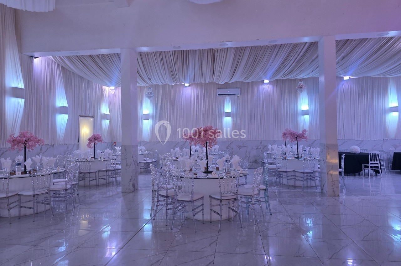 Salle de réception élégante avec tables rondes décorées de nappes blanches et centres de table roses, éclairage tamisé.
