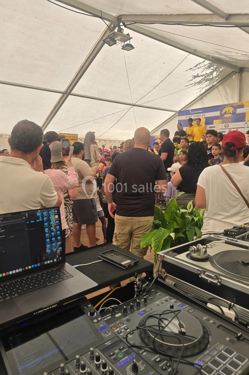 Vue depuis une table de mixage sur une foule rassemblée sous une tente lors d'un événement festif.