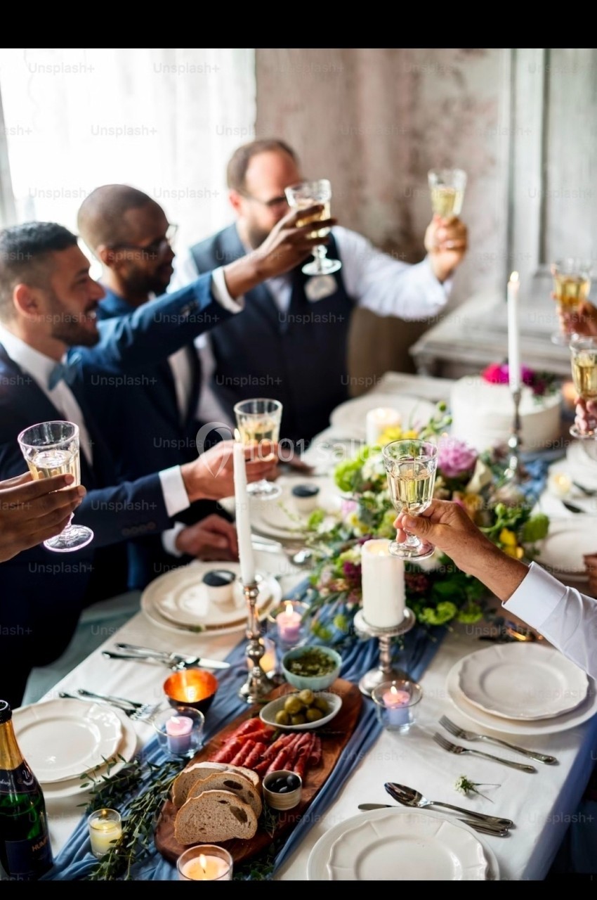 Des personnes trinquent autour d'une table élégamment dressée avec des bougies, des fleurs et des plats variés.