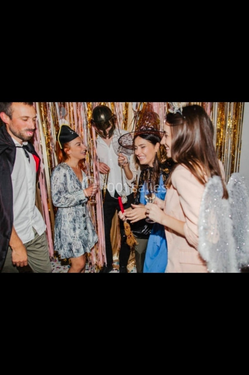 Des personnes déguisées discutent et rient lors d'une fête, devant un rideau de guirlandes dorées.